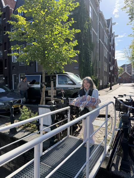 A woman with a cheerful smile crosses a small bridge over a canal, carrying a colorful bundle in Oudeschans, Uilenburg, Amsterdam